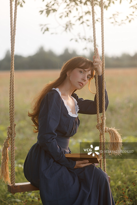 年轻女性在乡村秋千上阅读图片素材