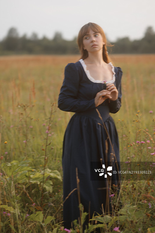 身穿帝国风格裙子的年轻女性站在田野中，乡村场景。历史服装，19世纪风格。图片素材