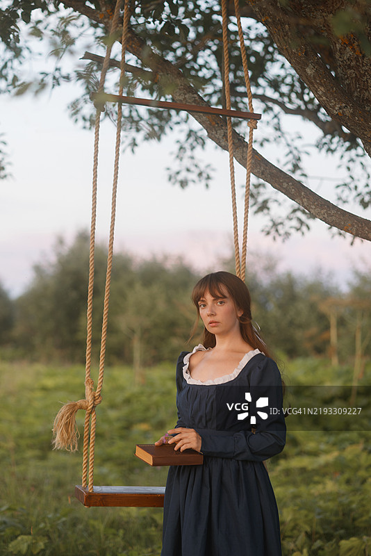 年轻女性在乡村秋千上阅读图片素材