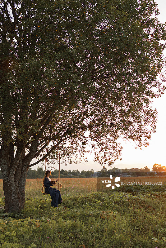 年轻女性在乡村秋千上阅读图片素材