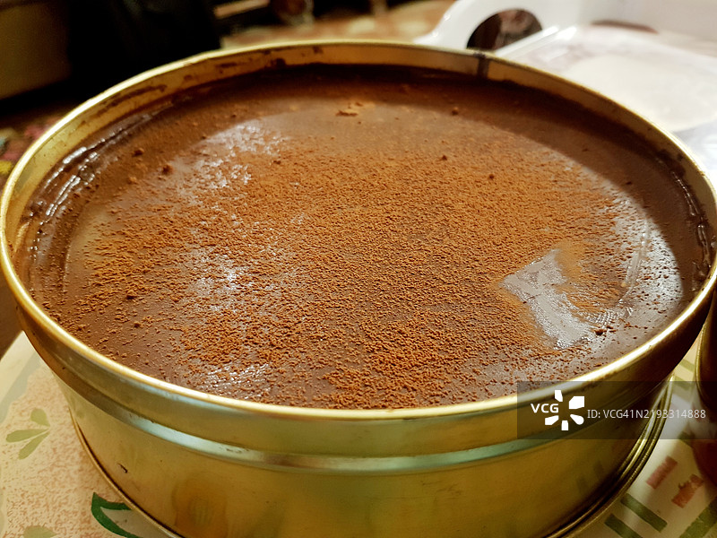 光滑奶油巧克力蛋糕，顶部覆盖坚硬巧克力，放在金色圆形烤盘中。图片素材