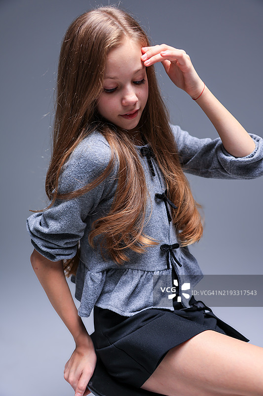 一位穿着灰色开衫的时尚女孩在摄影棚中优雅地为镜头摆姿势图片素材