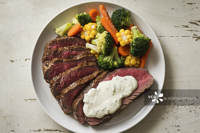 切片牛排上淋有奶油白酱，旁边配有混合蔬菜。图片素材