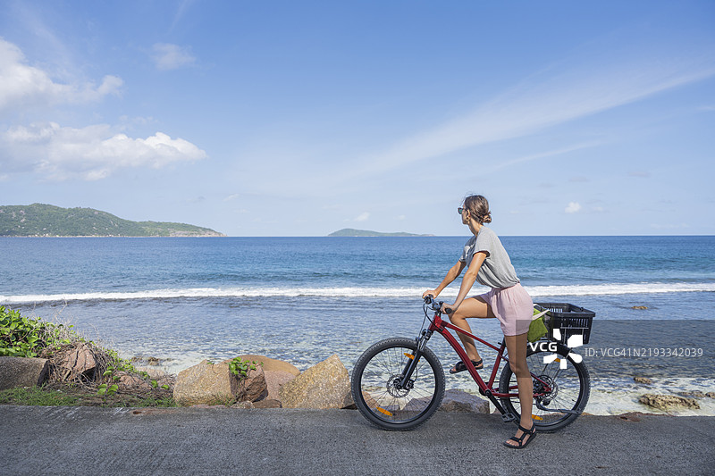 年轻女性骑自行车沿海边行驶图片素材