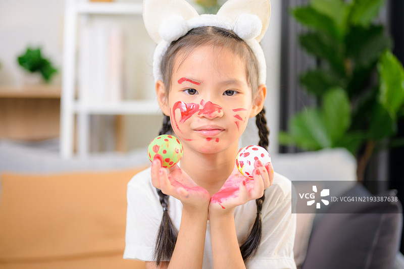 可爱的小女孩在复活节戴着兔耳朵。女孩坐在沙发上正在绘制复活节彩蛋。图片素材