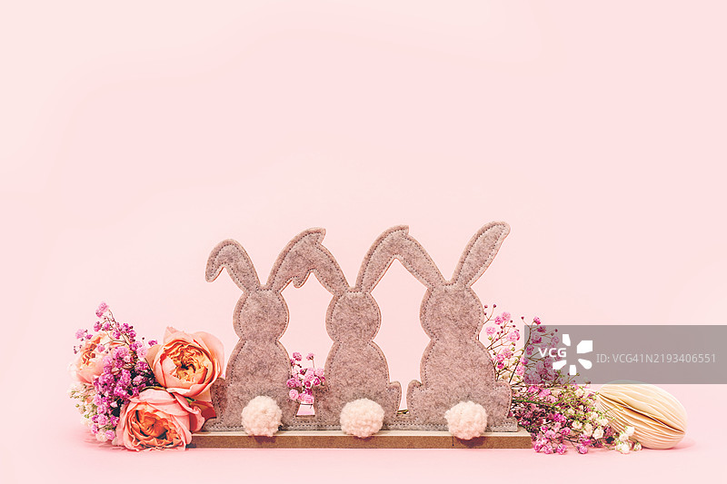 三个毛毡复活节兔子和粉色背景上的淡金色玫瑰花。图片素材