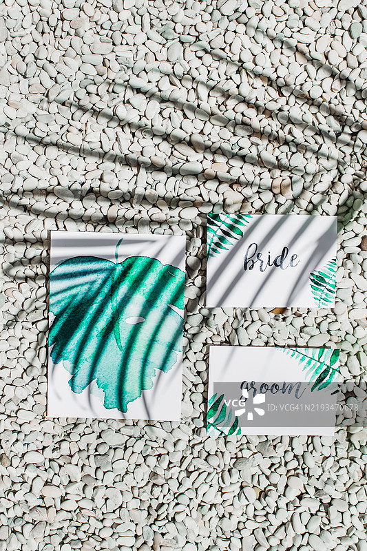 优雅的婚礼请柬，背景为白色卵石，映衬着棕榈叶的阴影图片素材