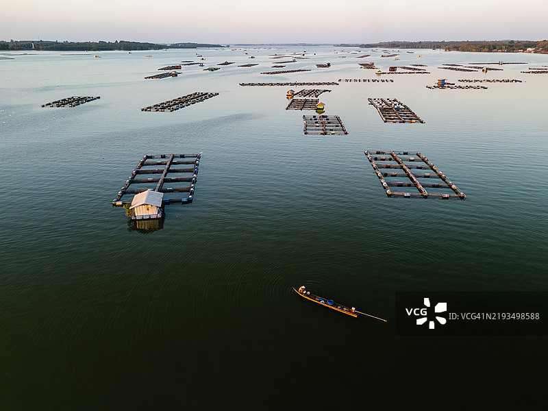 平静湖面上的漂浮鱼塘鸟瞰图，长尾船在柔和的光线下滑行。图片素材