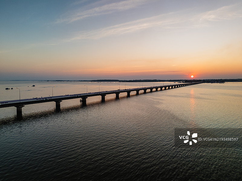 日落时分，长桥横跨宁静湖泊的鸟瞰图，鲜艳的色彩映照在平静的水面上。图片素材