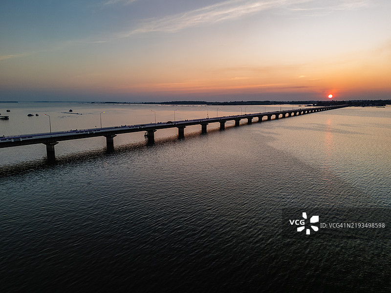 日落时分，长桥横跨宁静湖泊的鸟瞰图，鲜艳的色彩映照在平静的水面上。图片素材