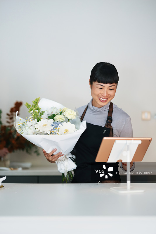 花店老板手持新鲜花束，在店铺柜台上使用平板电脑图片素材