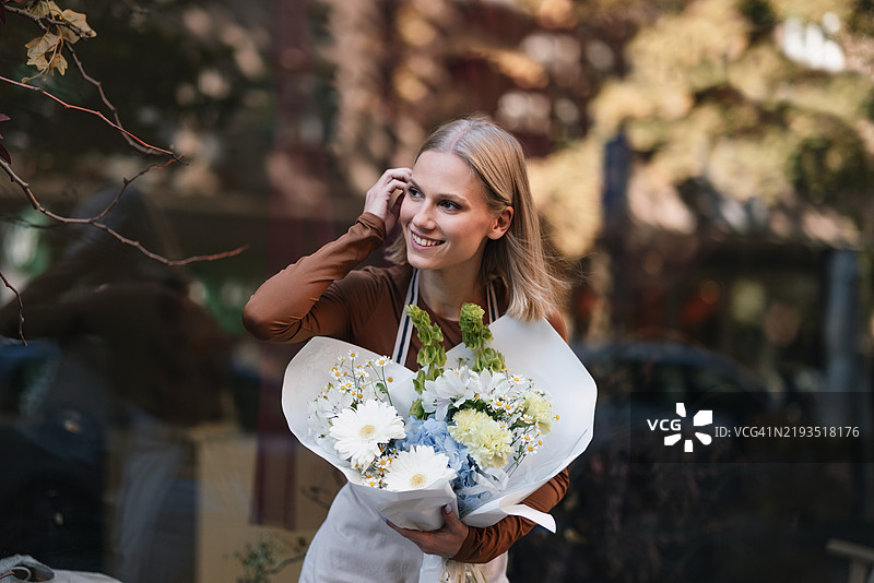 微笑的花店老板在秋天的户外提着美丽的花束图片素材