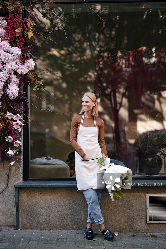 花店外站着的花店老板手里拿着一束新鲜的花束图片素材
