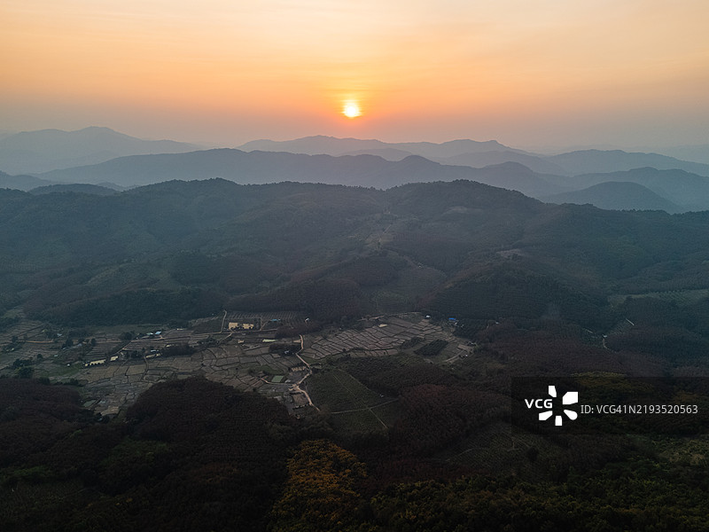 宁静的日落从空中照亮乡村农田，四周环绕着起伏的山丘和郁郁葱葱的绿地，构成一幅宁静的风景。图片素材