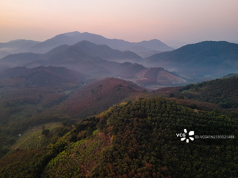 日出时分，宁静的鸟瞰图展示了被雾气笼罩的山脉，柔和的光线下绿意盎然的层叠山丘。图片素材