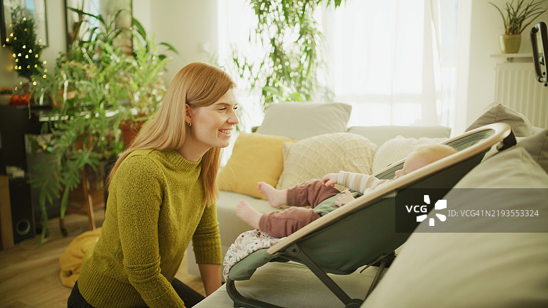 红发母亲握着宝宝的手，微笑着看着他。图片素材