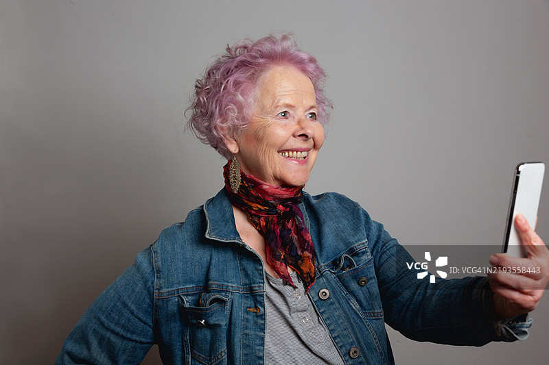 一位拥有粉色头发的老年女性正在用智能手机自拍图片素材