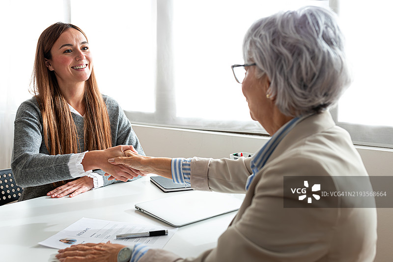 好交易。两位女商人在工作场所坐着握手。图片素材