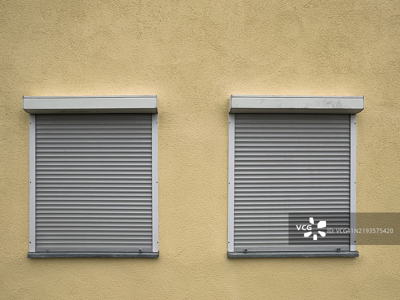 两扇关闭的百叶窗在黄色墙壁上图片素材