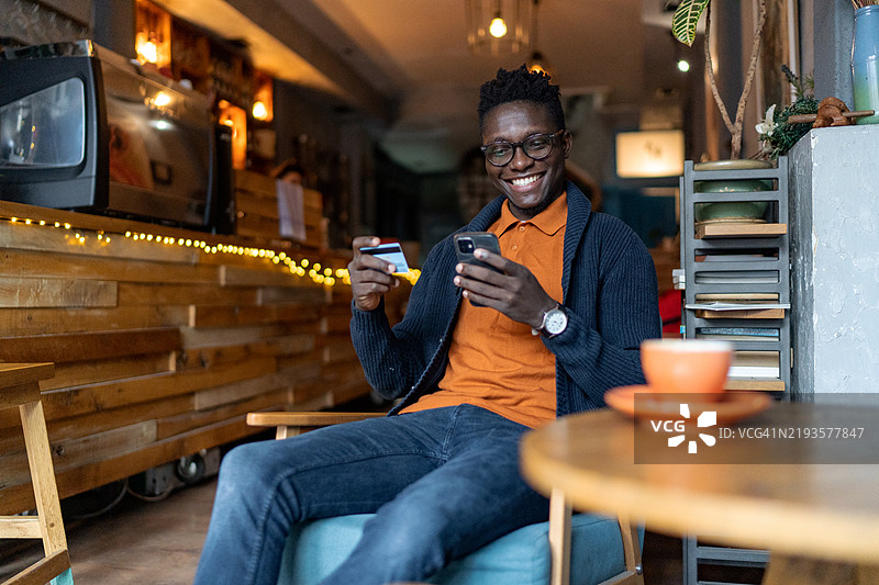 年轻男子坐在咖啡馆里，用手机和信用卡进行在线购物图片素材