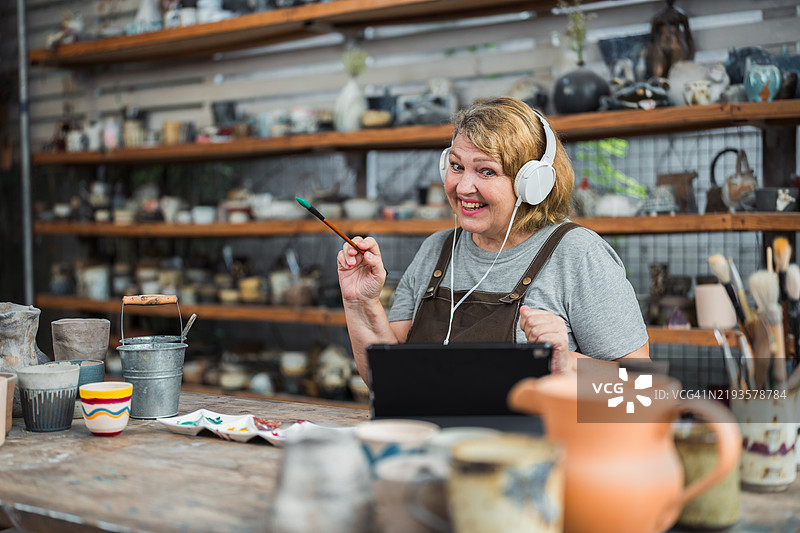 一位年长女性在参加陶艺绘画工作坊时正在进行视频通话图片素材