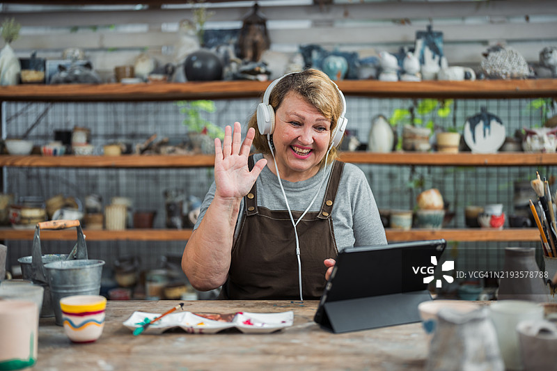 一位年长女性在参加陶艺绘画工作坊时正在进行视频通话图片素材