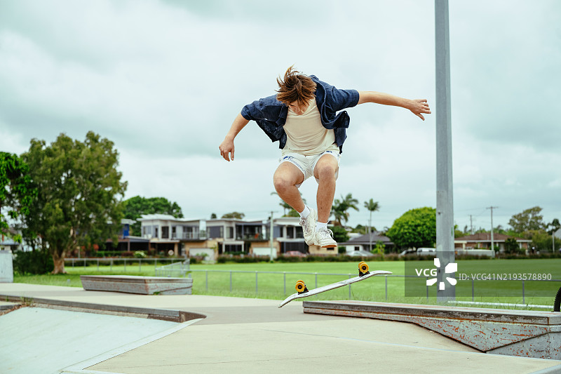 年轻的滑板运动员在户外滑板公园的半管上练习技巧，天气阴云密布。图片素材