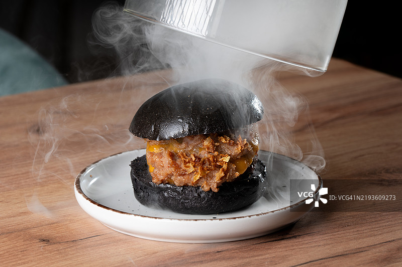 厨师在餐厅里将玻璃罩放在冒 steam 的黑色汉堡上图片素材