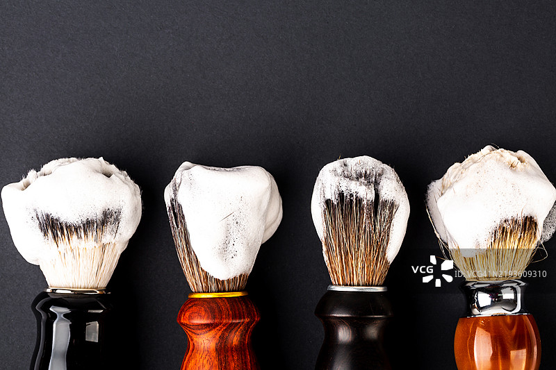 不同的剃须刷与黑色背景上的泡沫。图片素材