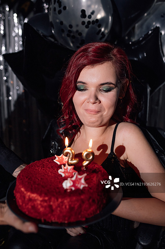年轻女性在节日气氛中庆祝生日，红色蛋糕和蜡烛环绕着装饰品。图片素材