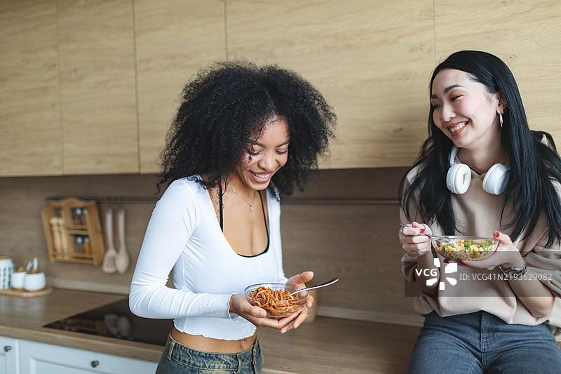 两个女性朋友在厨房里吃沙拉并聊天图片素材