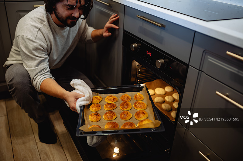 一个男人把一盘烘焙食品放在柜台上，朋友们在背景中聚集。温暖而迷人的场景捕捉了分享美食的快乐。图片素材