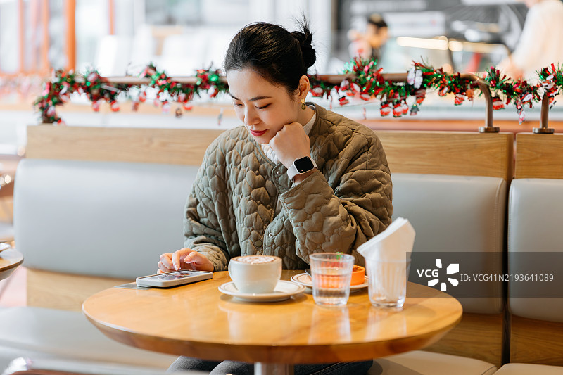 美丽的亚洲女性在酒店咖啡厅使用智能手机。享受下午的放松时光。咖啡休息。生活方式与科技。图片素材