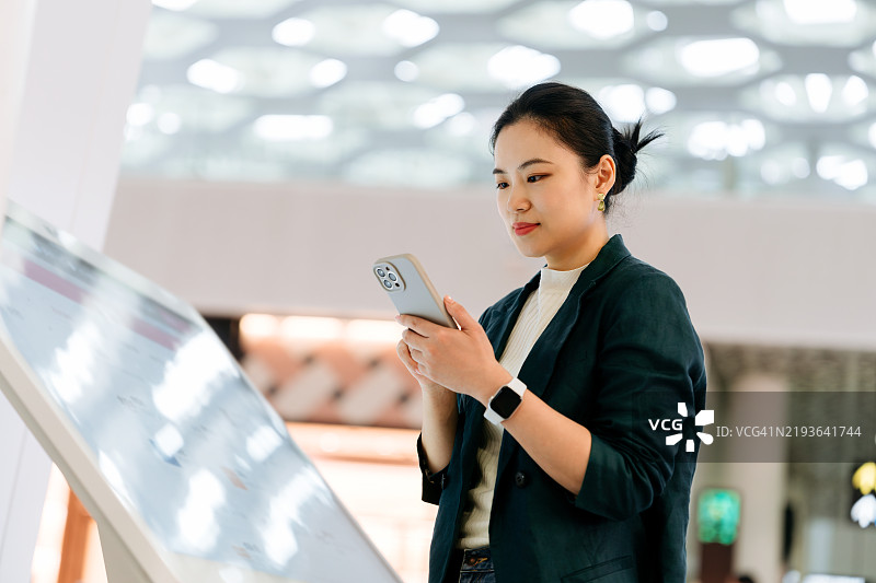 亚洲女商人在商店中使用智能手机并触摸自助设备的屏幕。设备商店导航器。自助购买。图片素材