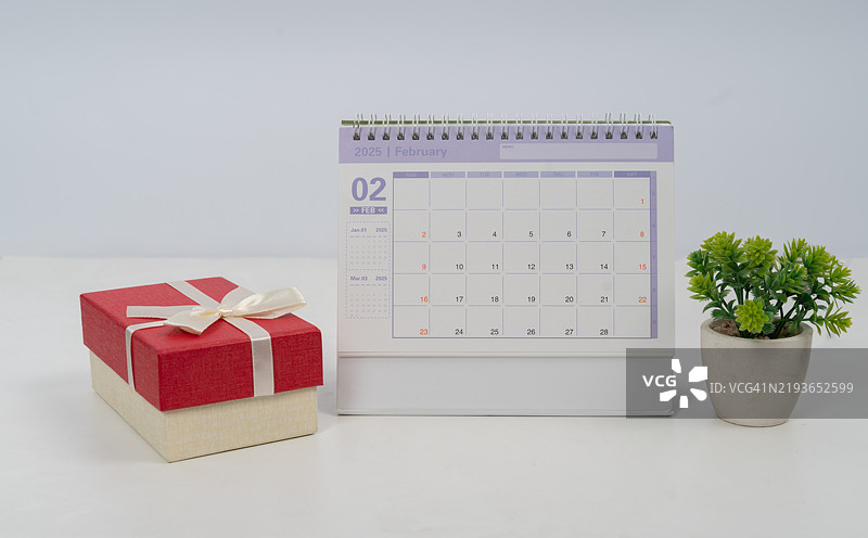 一个红色的盒子上系着白色的丝带，放在桌子上，旁边有一个日历。图片素材
