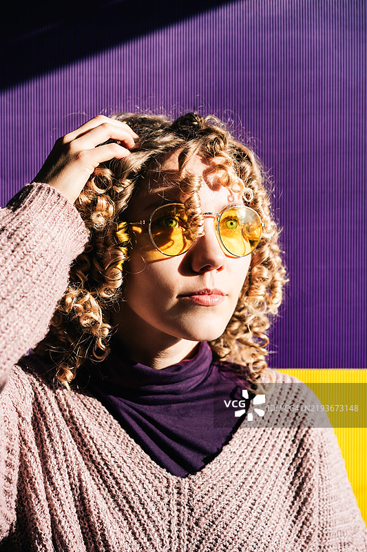 在温暖的光线下，微笑的女性与色彩斑斓的紫色和黄色背景相映成趣图片素材