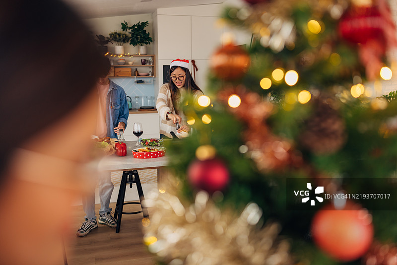 微笑的亚洲女性戴着圣诞老人帽子，在厨房准备圣诞午餐图片素材