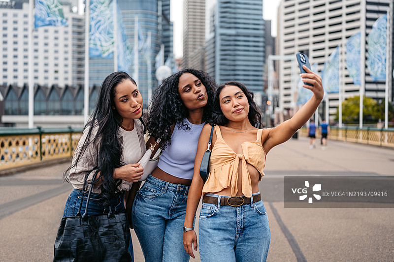 三位年轻女性朋友在澳大利亚悉尼的达令港一起用手机自拍图片素材