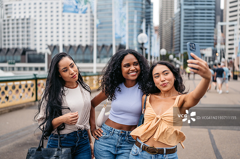 三位年轻女性朋友在澳大利亚悉尼的达令港一起用手机自拍图片素材