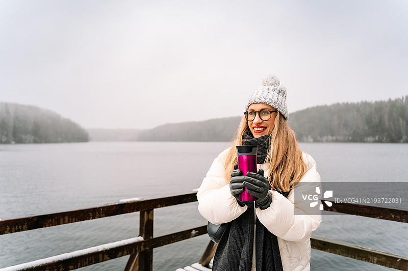 冬日里，年轻女子在雪-covered湖边拿着保温瓶图片素材