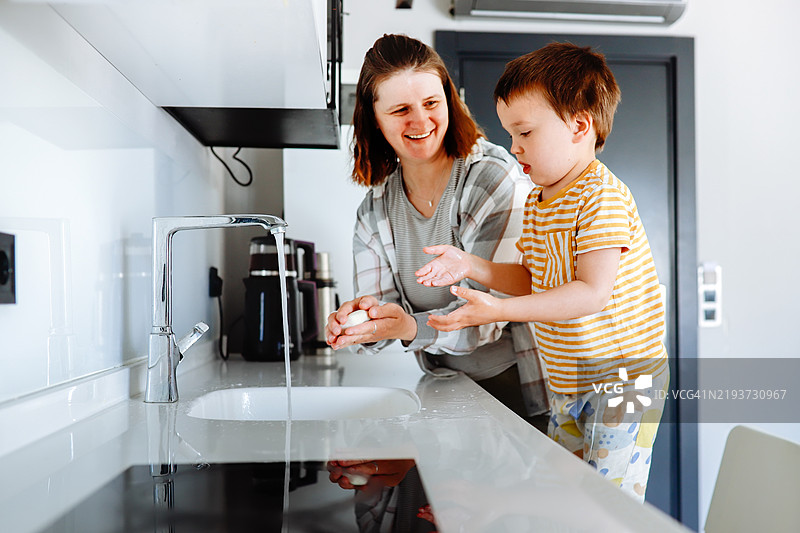 家庭时刻：丰满的妈妈和幼儿儿子在厨房用肥皂洗手。图片素材