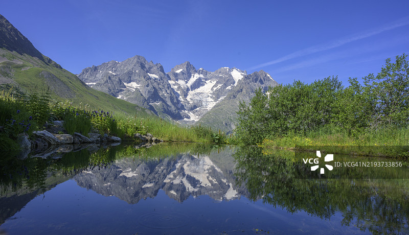 皮亚杰峰和拉梅耶峰倒映在法国高阿尔卑斯省维拉尔达雷纳的劳塔雷特植物园池塘中。图片素材
