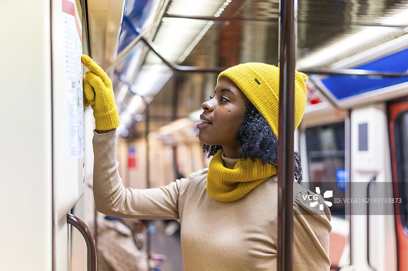 穿着黄色冬装的游客在地铁列车内查看地铁地图图片素材