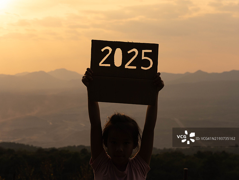 可爱小女孩在日落背景下举着2025标志的剪影，祝大家新年快乐2025图片素材