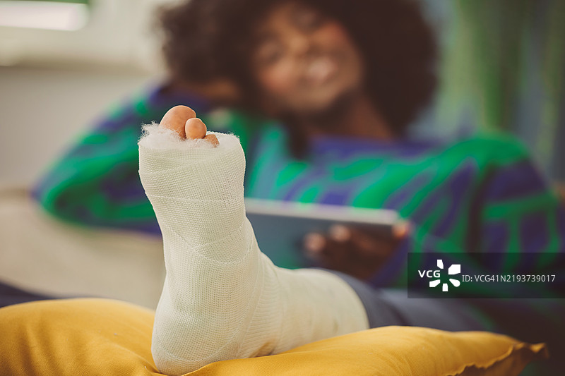 年轻女性在家中用iPad，腿部骨折。图片素材