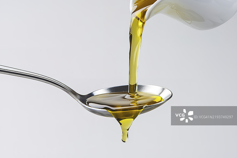 金黄色的食用油从白色容器中倒入金属勺子上图片素材