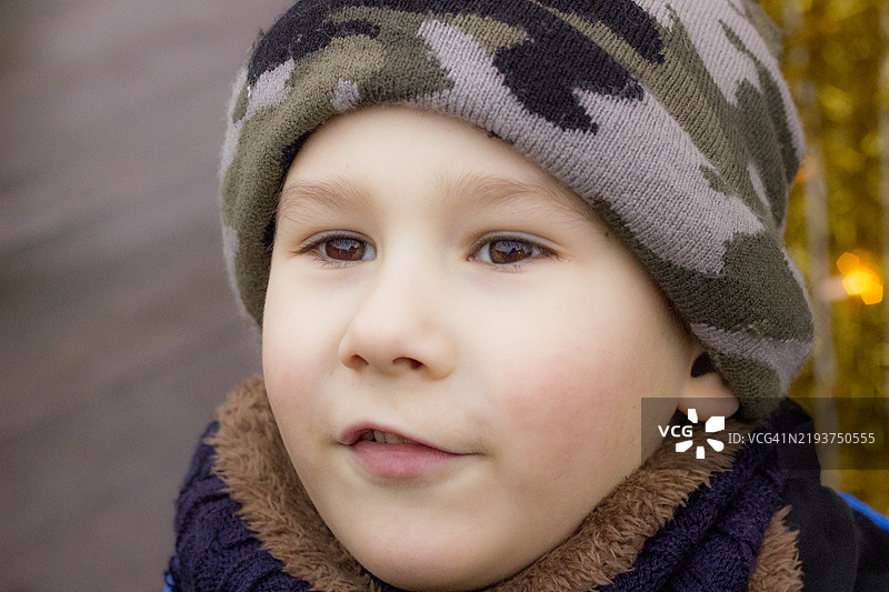 一个戴着迷彩帽、穿着保暖衣物的男孩在凉爽的天气中，面露沉思的表情图片素材