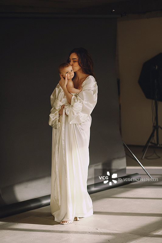 母亲在黑色背景的摄影棚中亲吻她的女婴，展现快乐的母亲身份概念图片素材