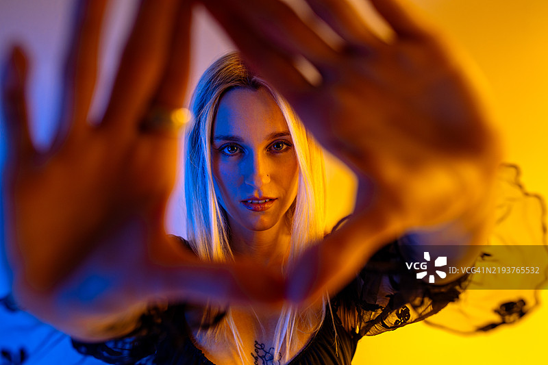 女人用手形成三角形框住自己的脸，沐浴在蓝色和橙色的光线中图片素材