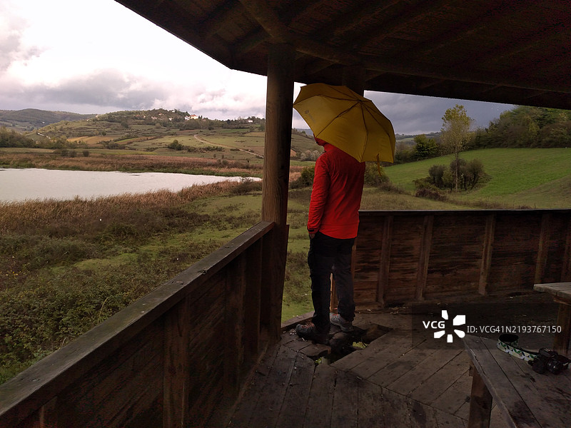 背影男子手持雨伞站在栏杆旁图片素材